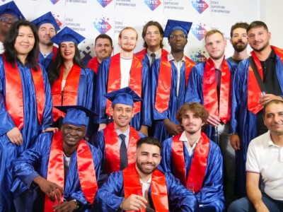 Groupe d'étudiants diplômés en informatique, portant des toges et toques bleues avec des écharpes rouges, posant ensemble lors d'une cérémonie de remise de diplômes. Ils sourient pour célébrer leur réussite académique.